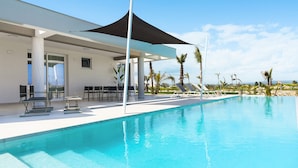 A modern pool area with a covered seating area, lounge chairs, and palm trees.