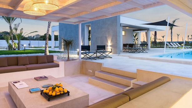 A modern outdoor living area with a pool, comfortable seating, and a staircase leading to a covered patio.