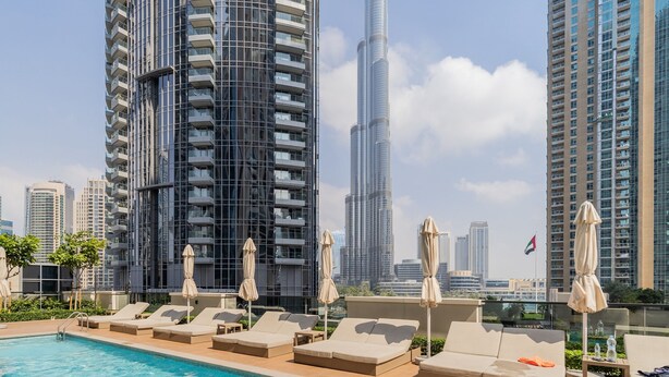 A rooftop pool with lounge chairs and umbrellas, surrounded by high-rise buildings and a clear sky. - EDEN'S Homes & Villas - Act One Act Two (Dubai)