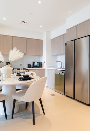 A modern kitchen with light wood cabinets, stainless steel appliances, and a white dining area with a marble table and chairs.