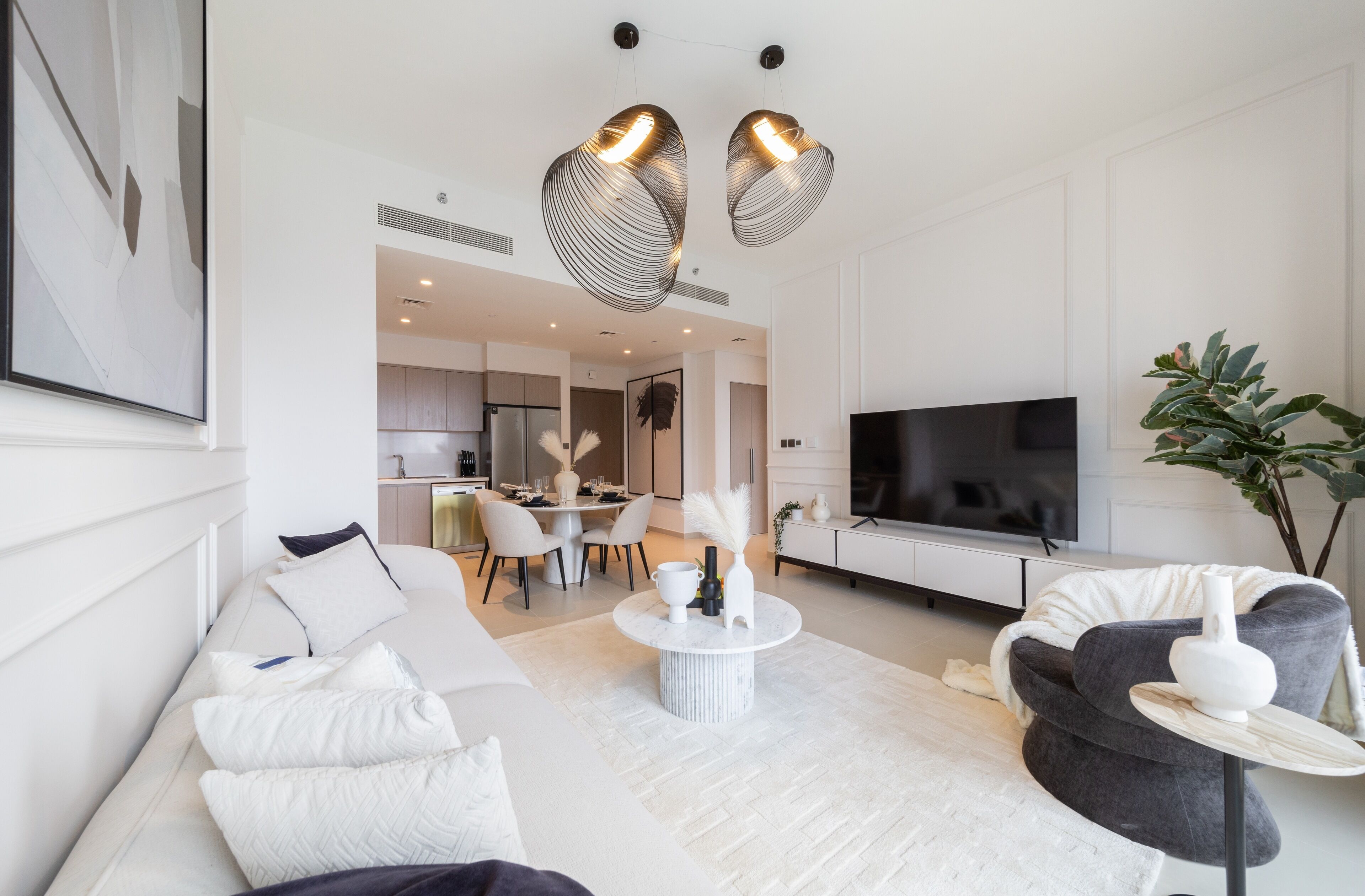 A modern living room with a sofa, a coffee table, a TV, and a dining area in the background.