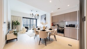 A modern kitchen with a dining area, featuring a round table, chairs, and a view of the city through large windows. - EDEN'S Homes & Villas - Act One Act Two (Dubai)
