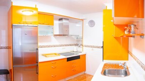 Une cuisine avec des meubles de couleur orange, un réfrigérateur en acier inoxydable, un évier et un four à micro-ondes.