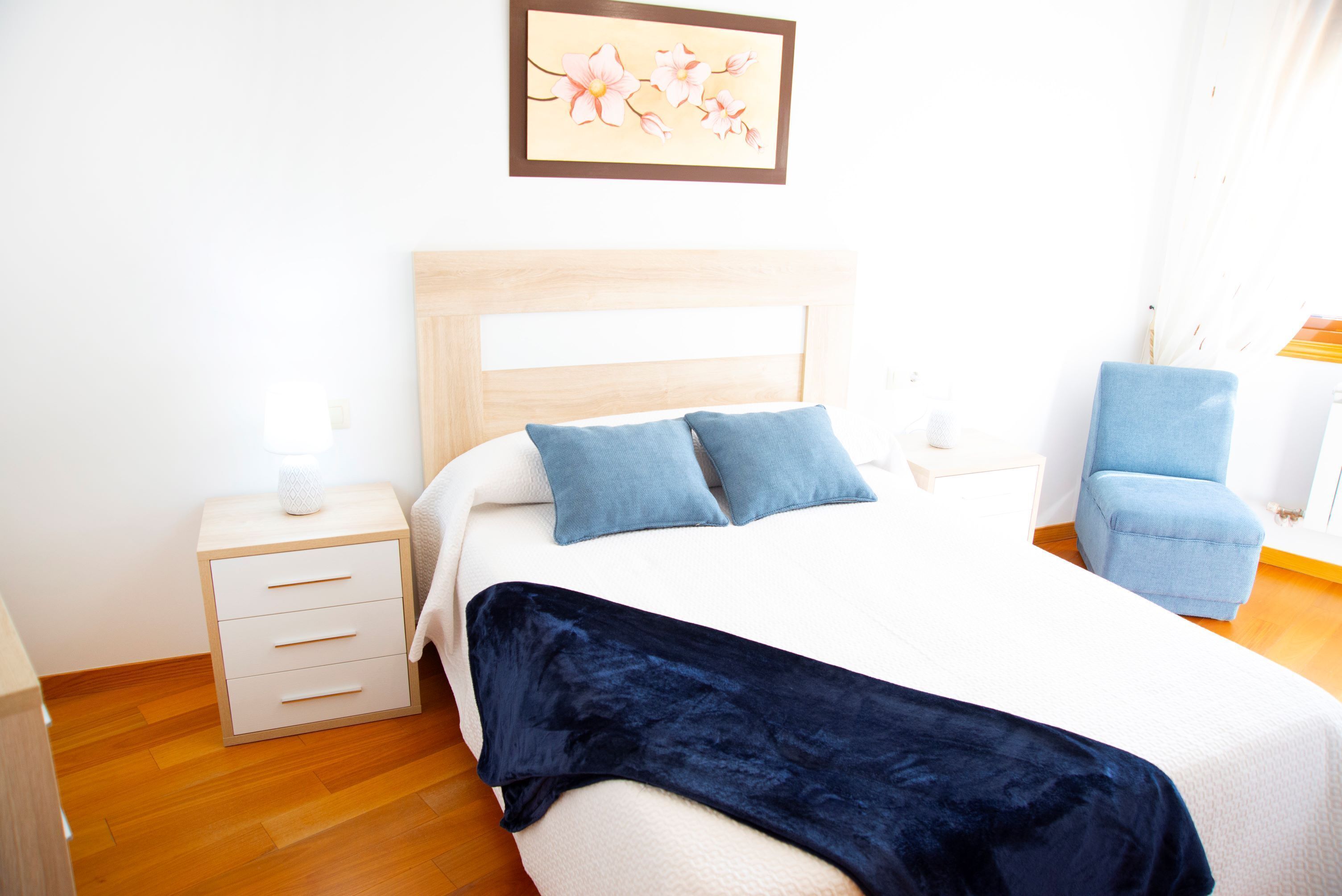 Een netjes ingerichte slaapkamer met een bed, nachtkastje, stoel en een wanddecoratie.