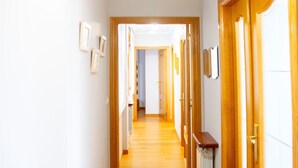 Un couloir doté de planchers et de portes en bois, qui mène à une pièce avec un radiateur et une fenêtre.