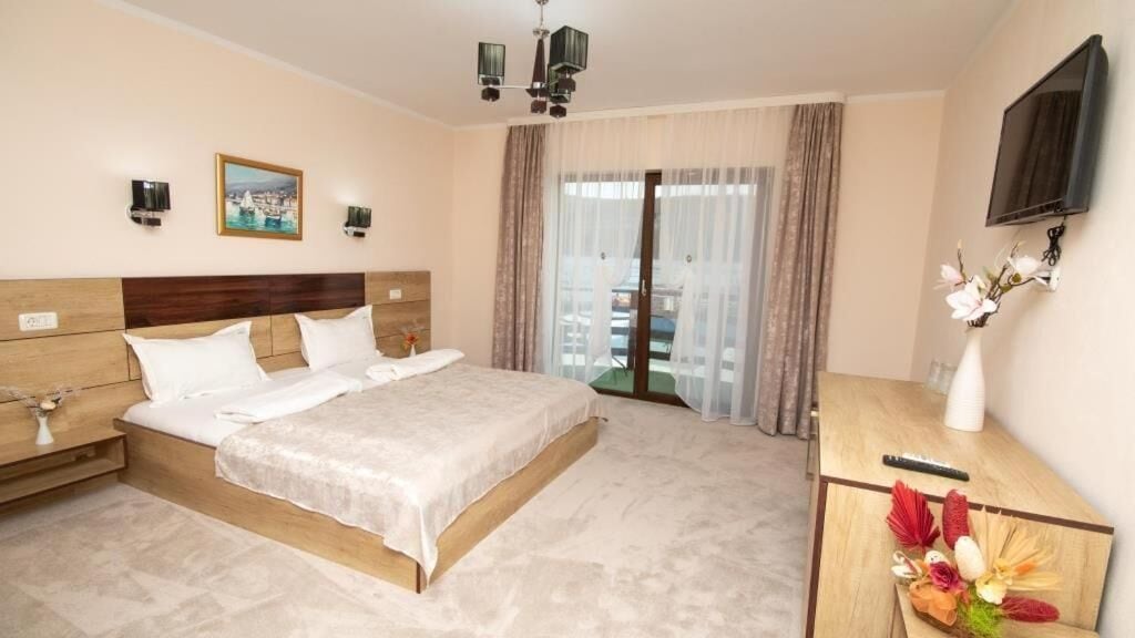 A hotel room with a large bed, bedside tables, a desk with a chair, a flat-screen TV, and a window with curtains.