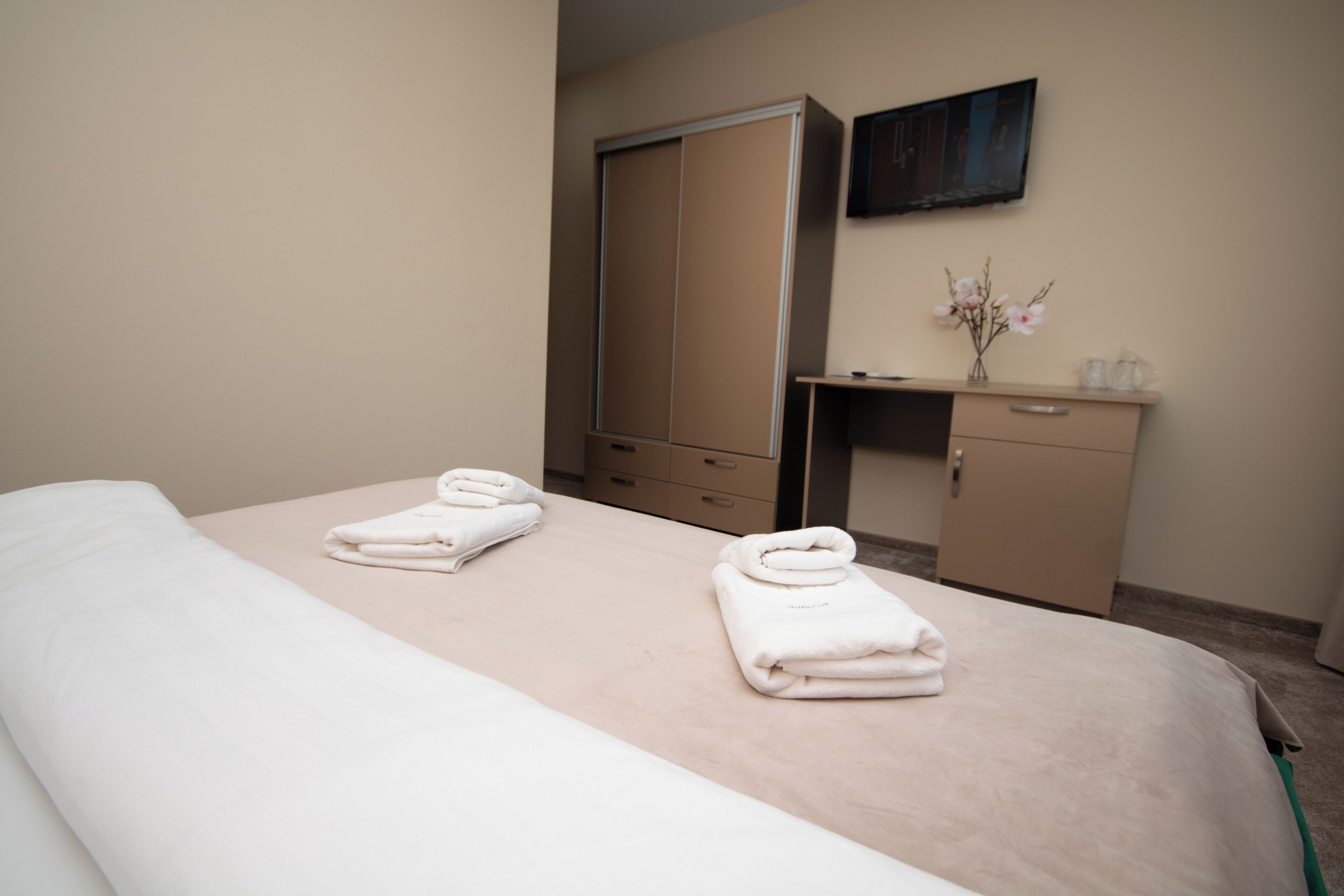 A hotel room with a bed, a desk, a wardrobe, and a flat-screen TV mounted on the wall.
