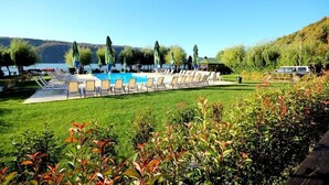 Ein Poolbereich mit Liegestühlen und Sonnenschirmen, umgeben von viel Grün und Blick auf Hügel.