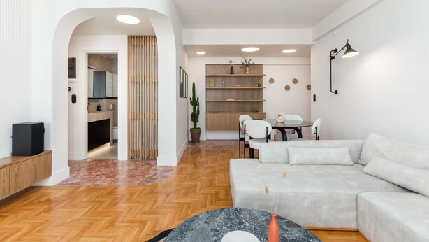 Una sala de estar moderna con un sofá, una mesa de comedor con sillas, una zona de cocina y una estantería.