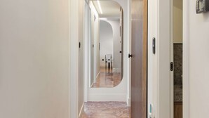 Un pasillo moderno con piso de piedra pulida, una puerta corredera y un espejo que refleja el espacio.