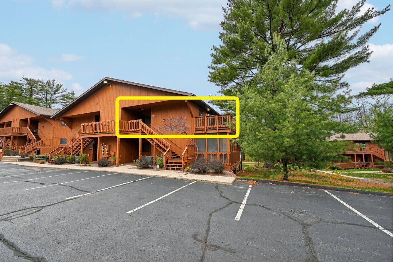 Un chalet en bois doté d’un balcon, d’un parking et entouré d’arbres.