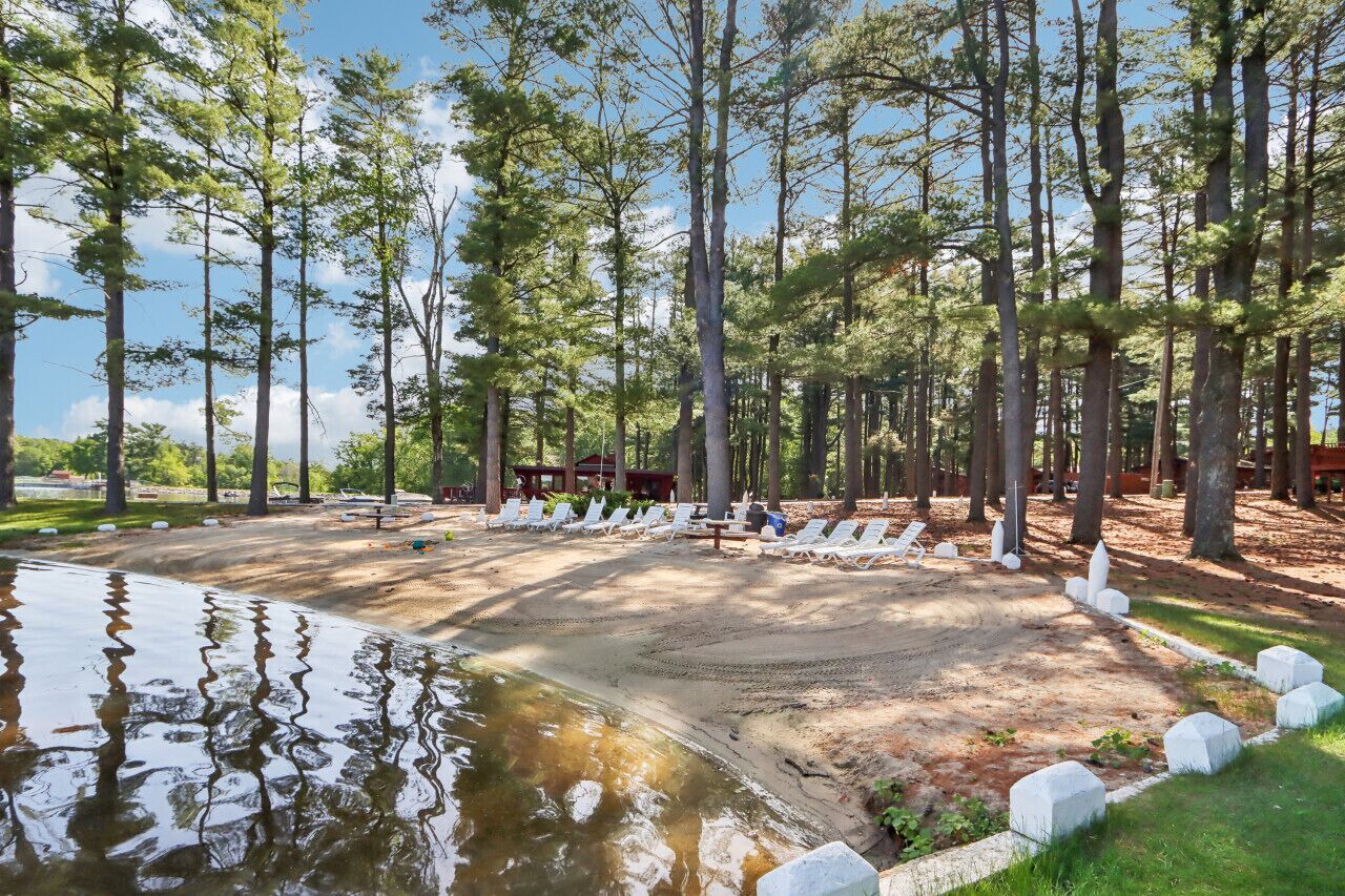 A sandy beach area with white lounge chairs and a small pond.