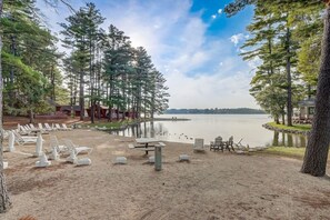 Una propiedad frente al lago con playa de arena, sillas de descanso, una mesa de picnic y un edificio tipo cabaña.