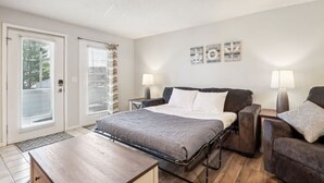Une chambre à coucher comprenant un lit, deux tables de chevet, un ventilateur de plafond et une fenêtre avec des stores.