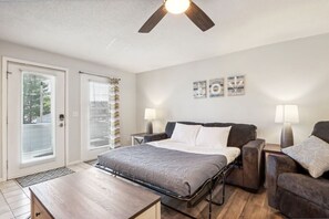 Un dormitorio con cama, dos mesitas de noche, ventilador de techo y ventana con persianas.
