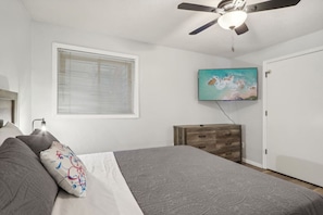 A bedroom with a bed, a ceiling fan, a dresser, a TV mounted on the wall, and a window with blinds. - Dreamy Dells Oasis for Families & Couples (Wisconsin Dells)