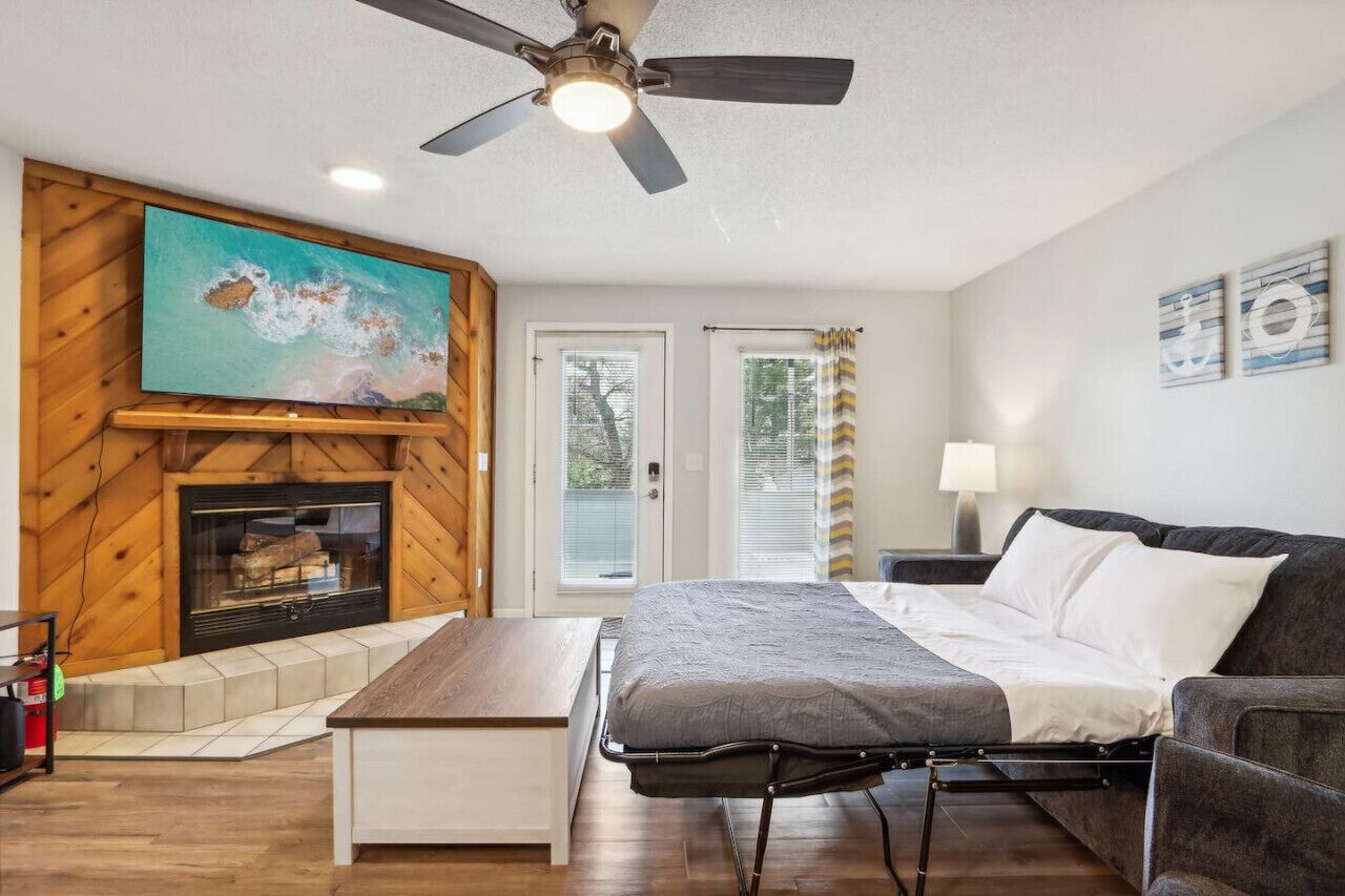 A room with a bed, a ceiling fan, a fireplace, and a large painting on the wall.