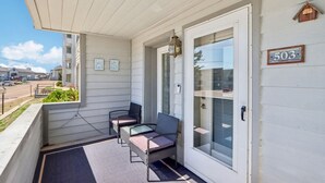 Un porche couvert avec deux chaises et une table, une porte avec un numéro, et une vue sur la rue.