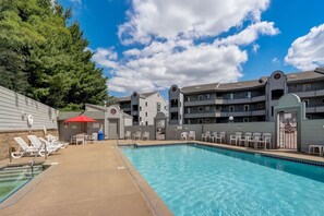 A swimming pool with lounge chairs and a red umbrella, surrounded by multi-story buildings with balconies. - Dreamy Dells Oasis for Families & Couples (Wisconsin Dells)