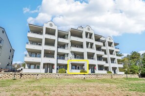 A multi-story residential building with balconies, a stone retaining wall, and a grassy area in front. - Dreamy Dells Oasis for Families & Couples (Wisconsin Dells)