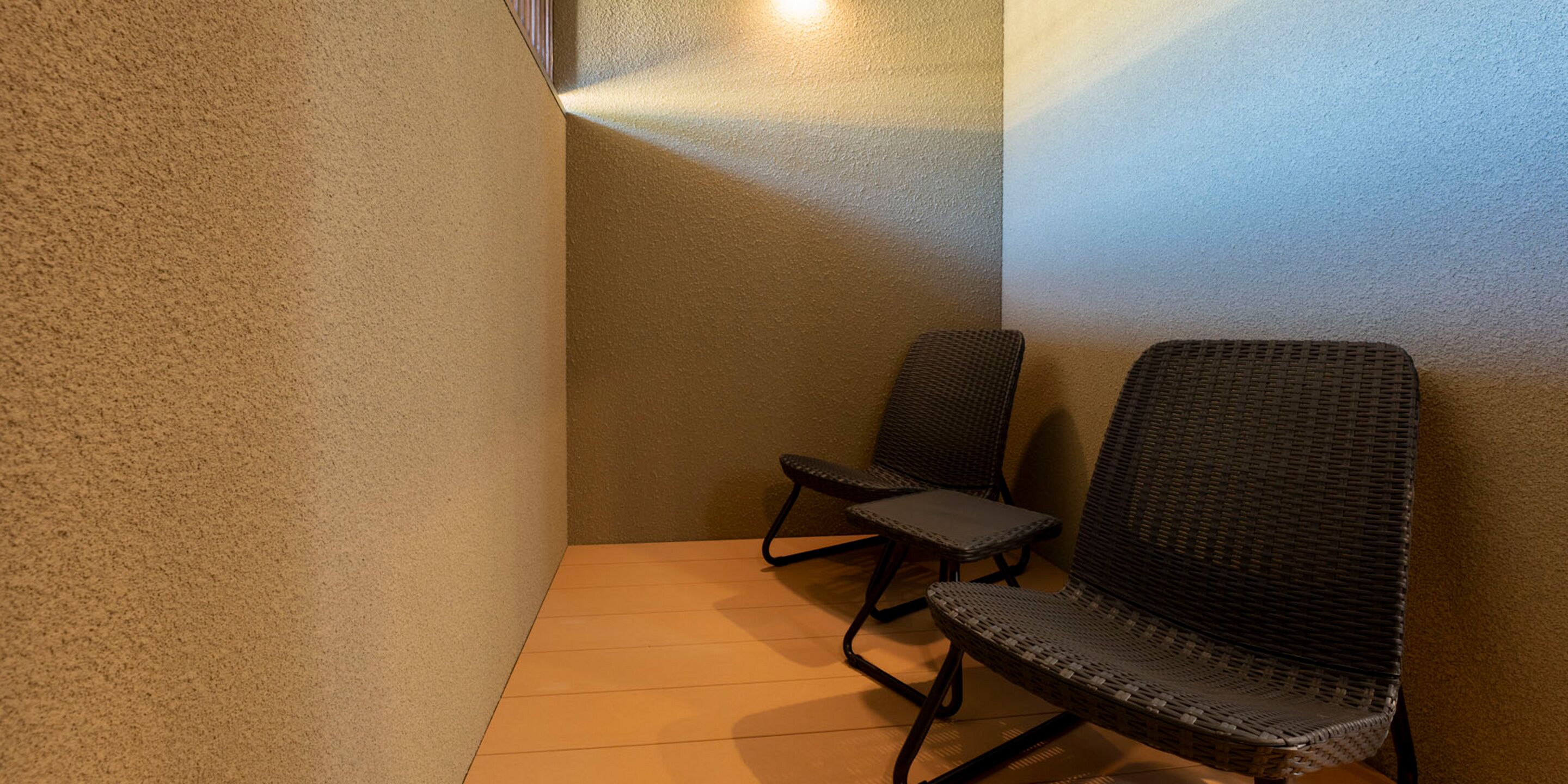 A corner of a room with two wicker chairs and a wooden floor.