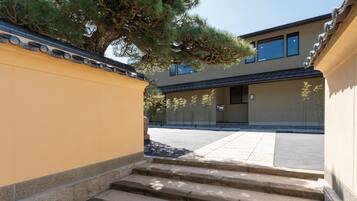 A building with a yellow exterior, a stone staircase, and a large tree in front.
