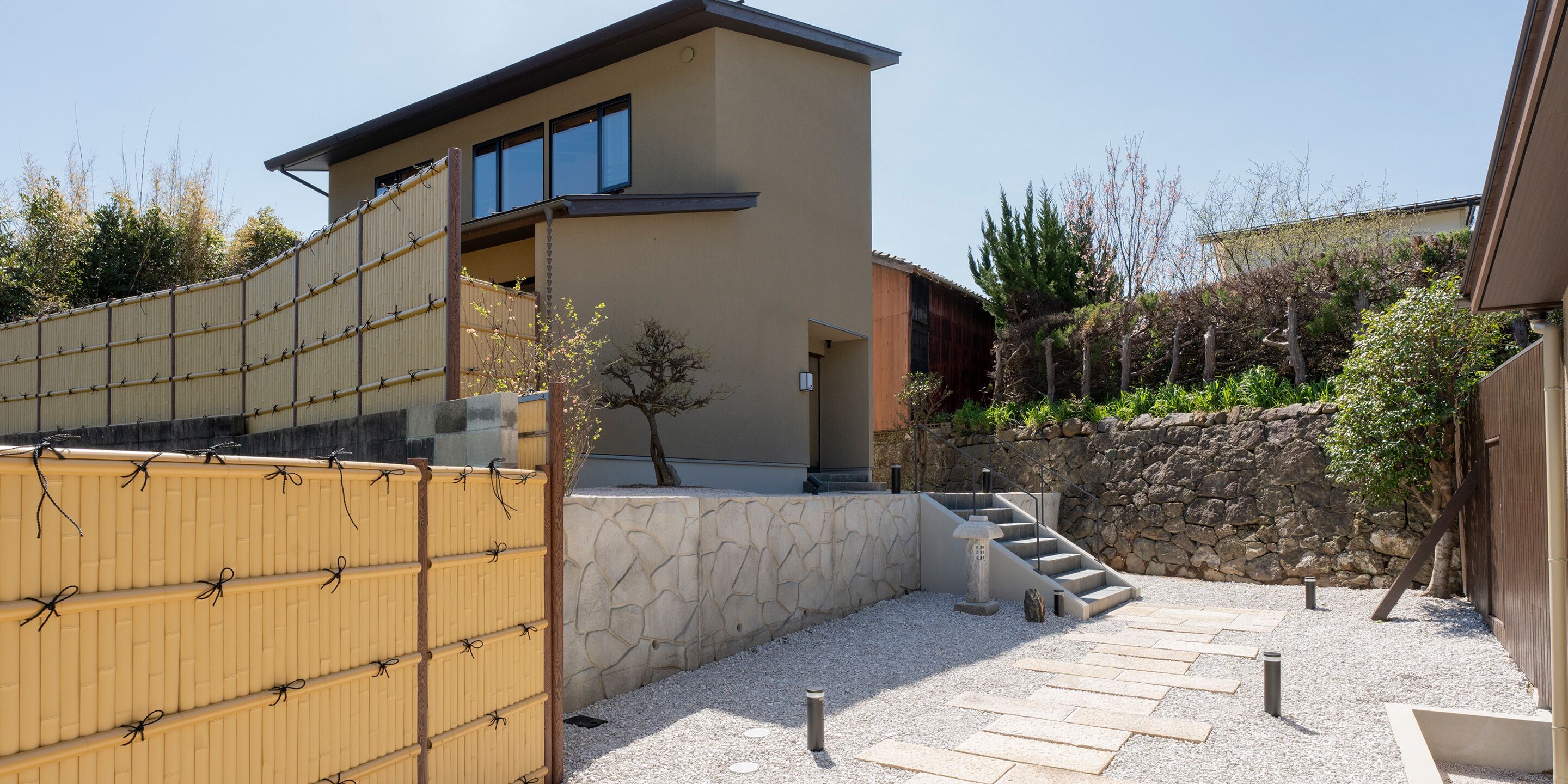 A modern building with a stone wall, a wooden fence, and a stone staircase leading to a door.