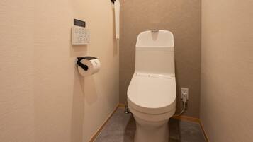 A small bathroom with a toilet, a paper towel dispenser, and a wall-mounted calendar.
