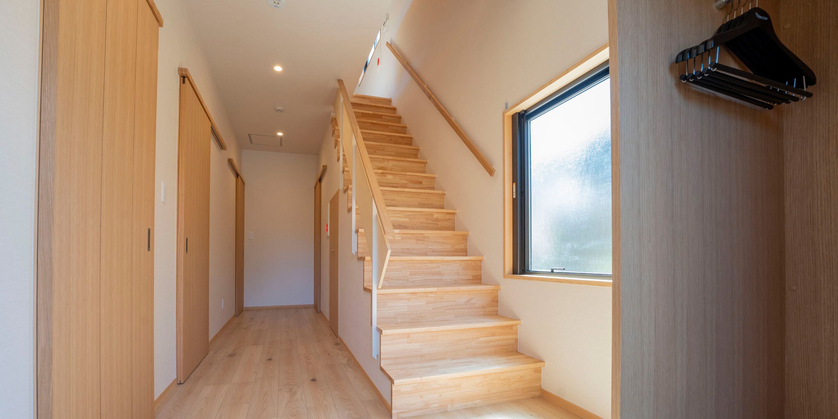 Un estrecho pasillo con suelo y escalera de madera que conduce a una habitación con un amplio ventanal.