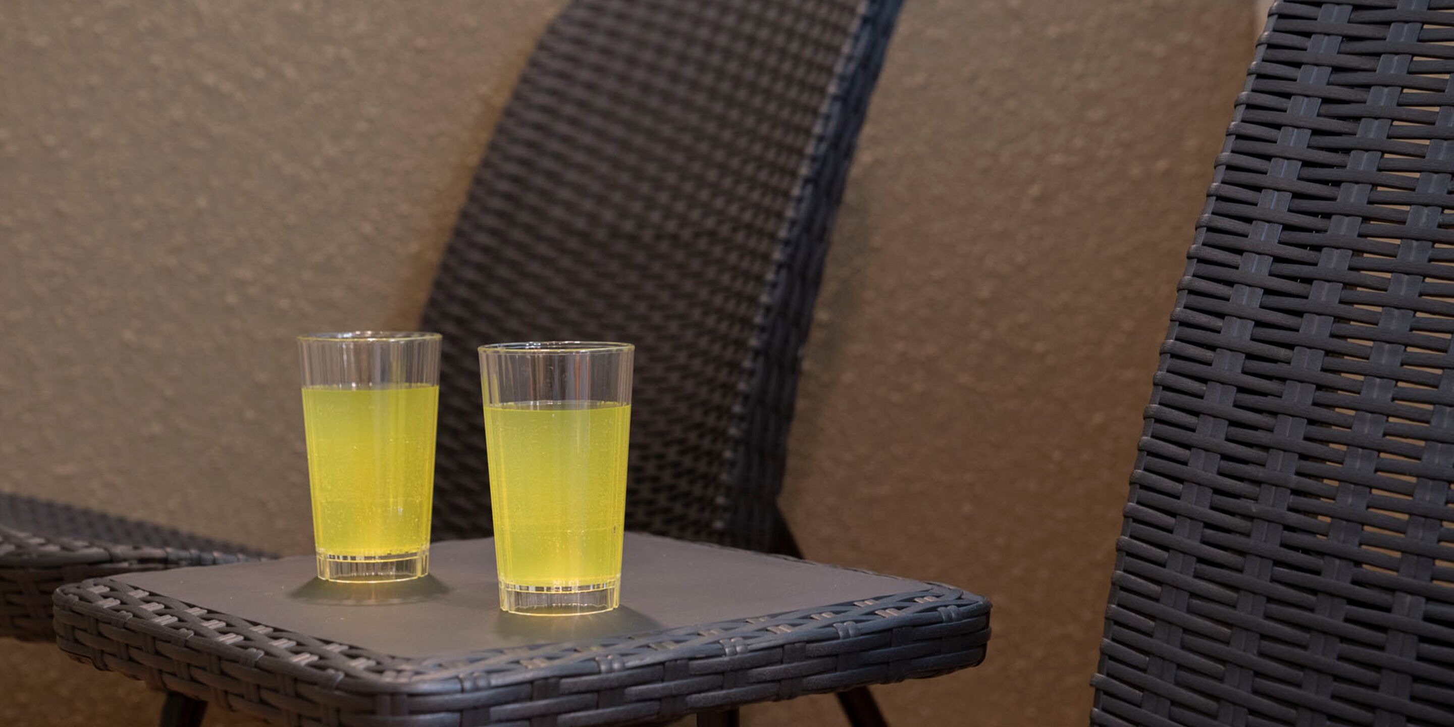 Zwei Gläser mit gelber Flüssigkeit auf einem Korbstuhl.