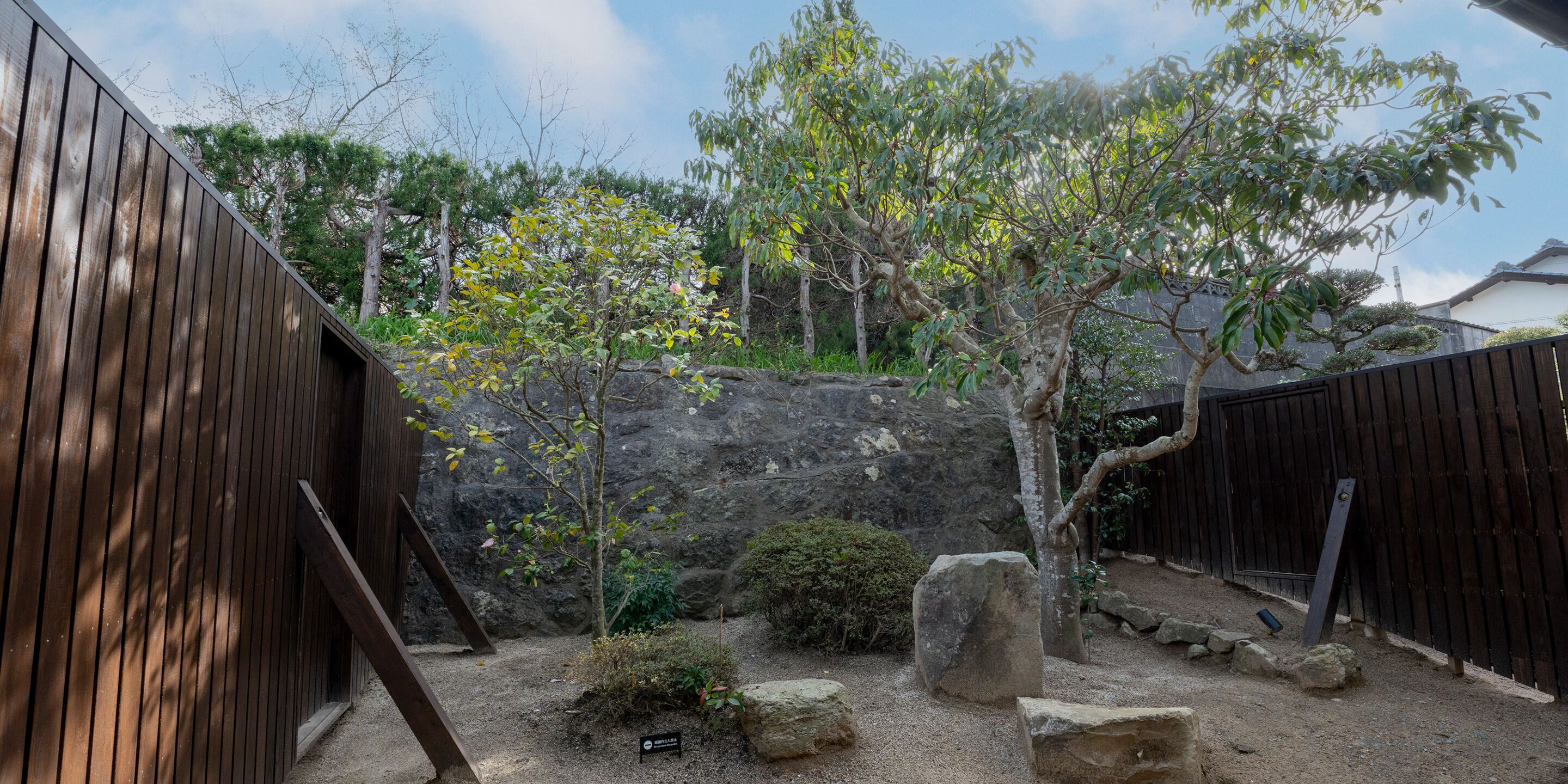 A garden with a wooden fence, a small tree, and a rocky backdrop.