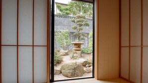 Habitació japonesa tradicional amb sòls de tatami, un panell shoji i vista a un jardí exterior amb un fanal de pedra i bonsais.