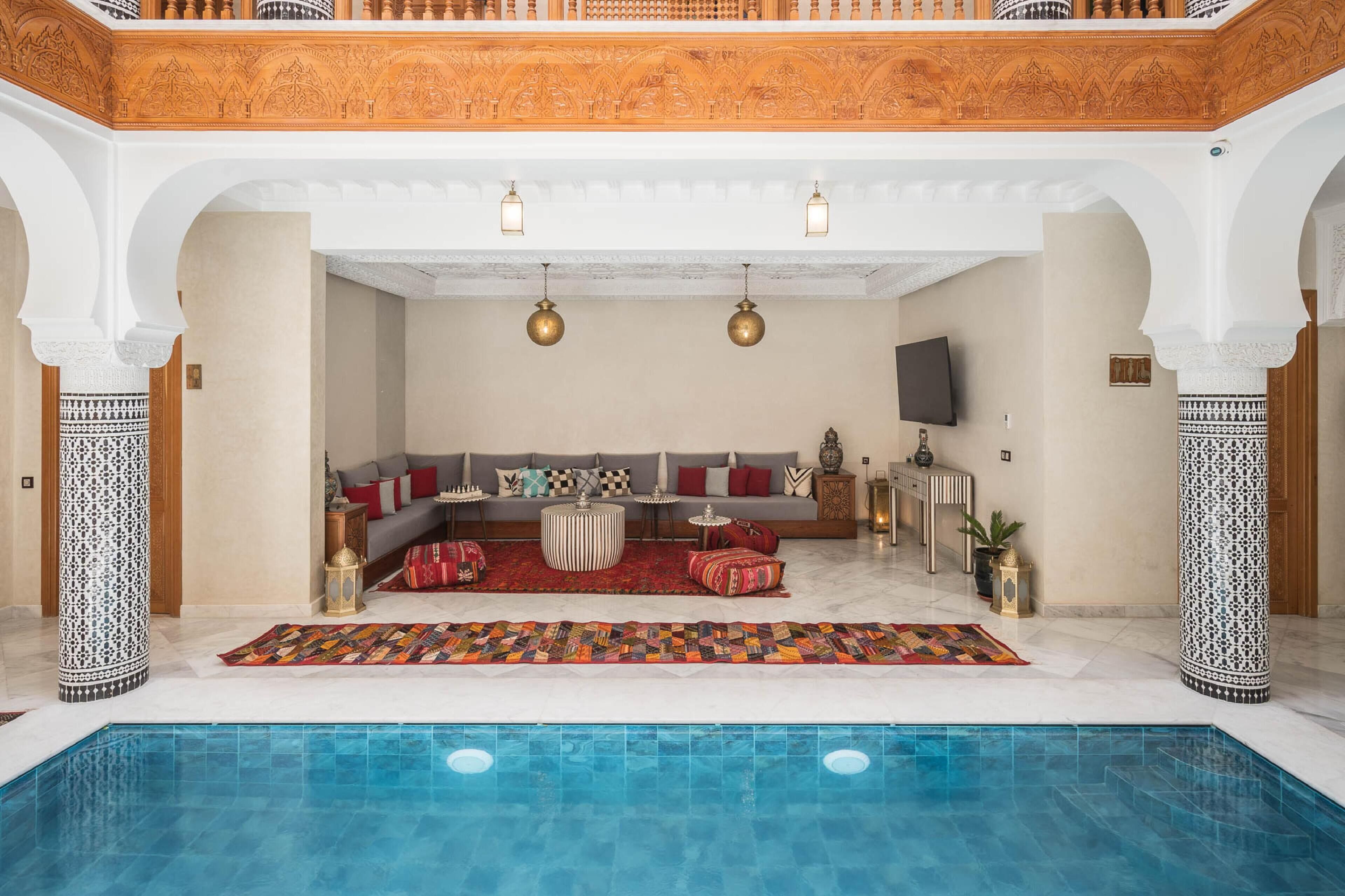 Un área de piscina interior lujosa con zona de estar, alfombra estampada y decoración tradicional.