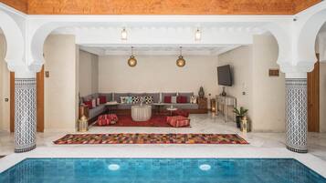 Un área de piscina interior lujosa con zona de estar, alfombra estampada y decoración tradicional.