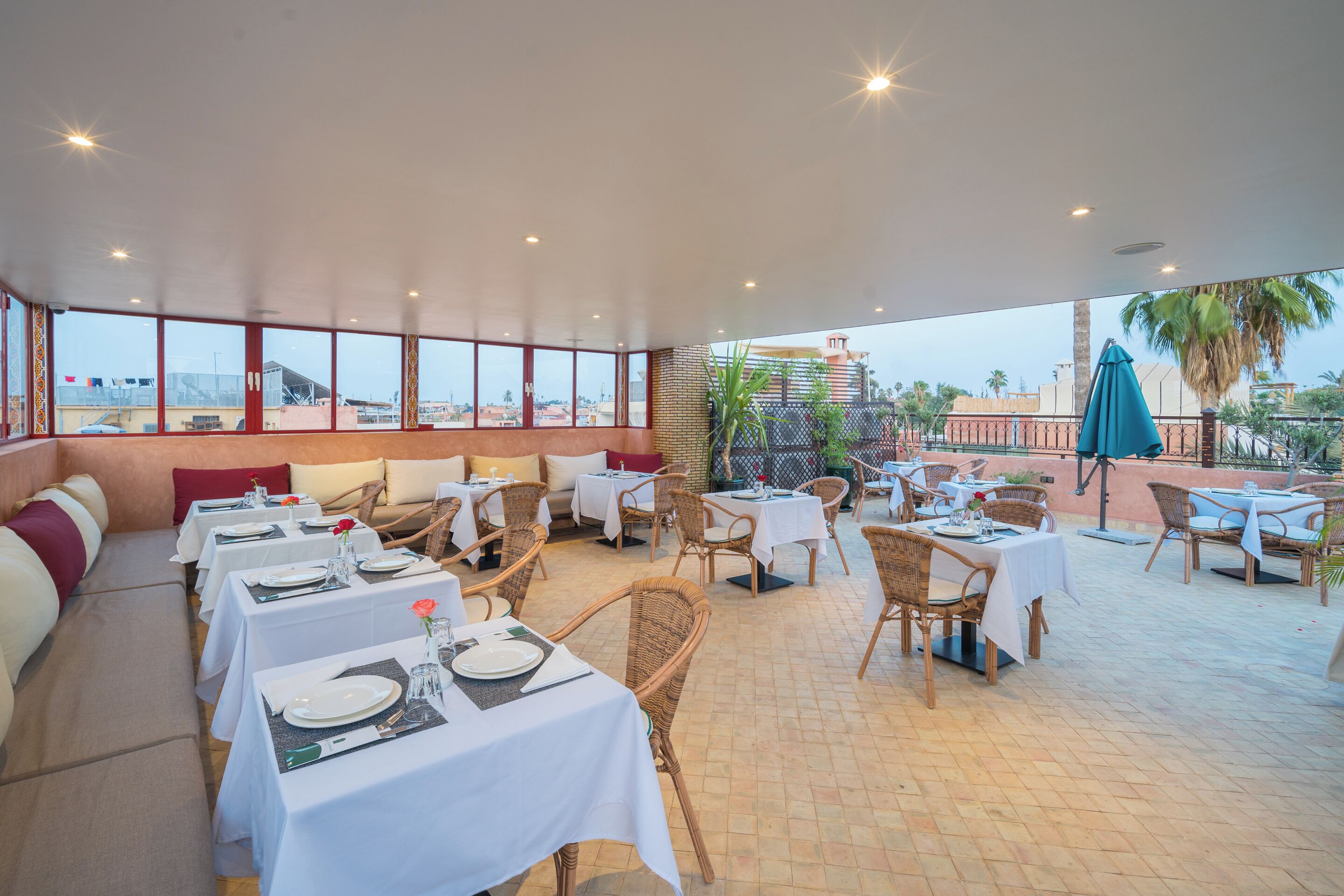 A restaurant with outdoor seating, white tablecloths, wicker chairs, and a view of the cityscape.