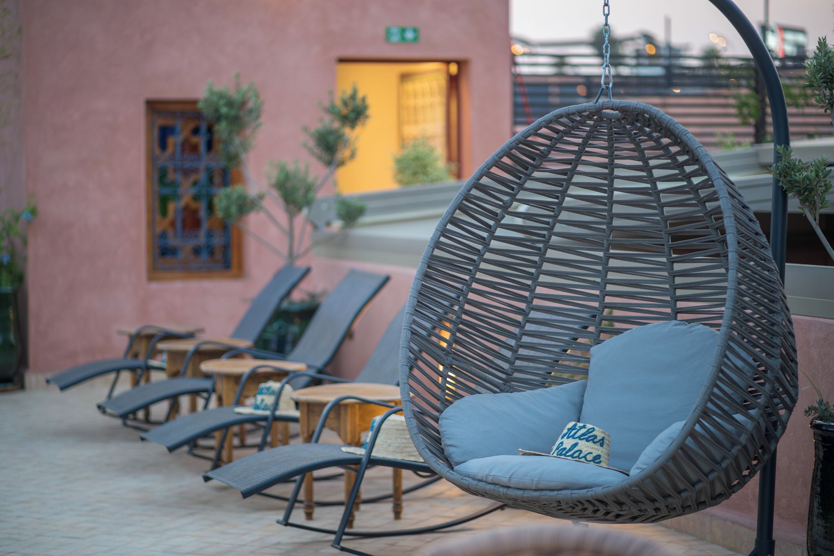 A hanging chair with a cushion, a wooden table, and a chair with a cushion in an outdoor seating area.