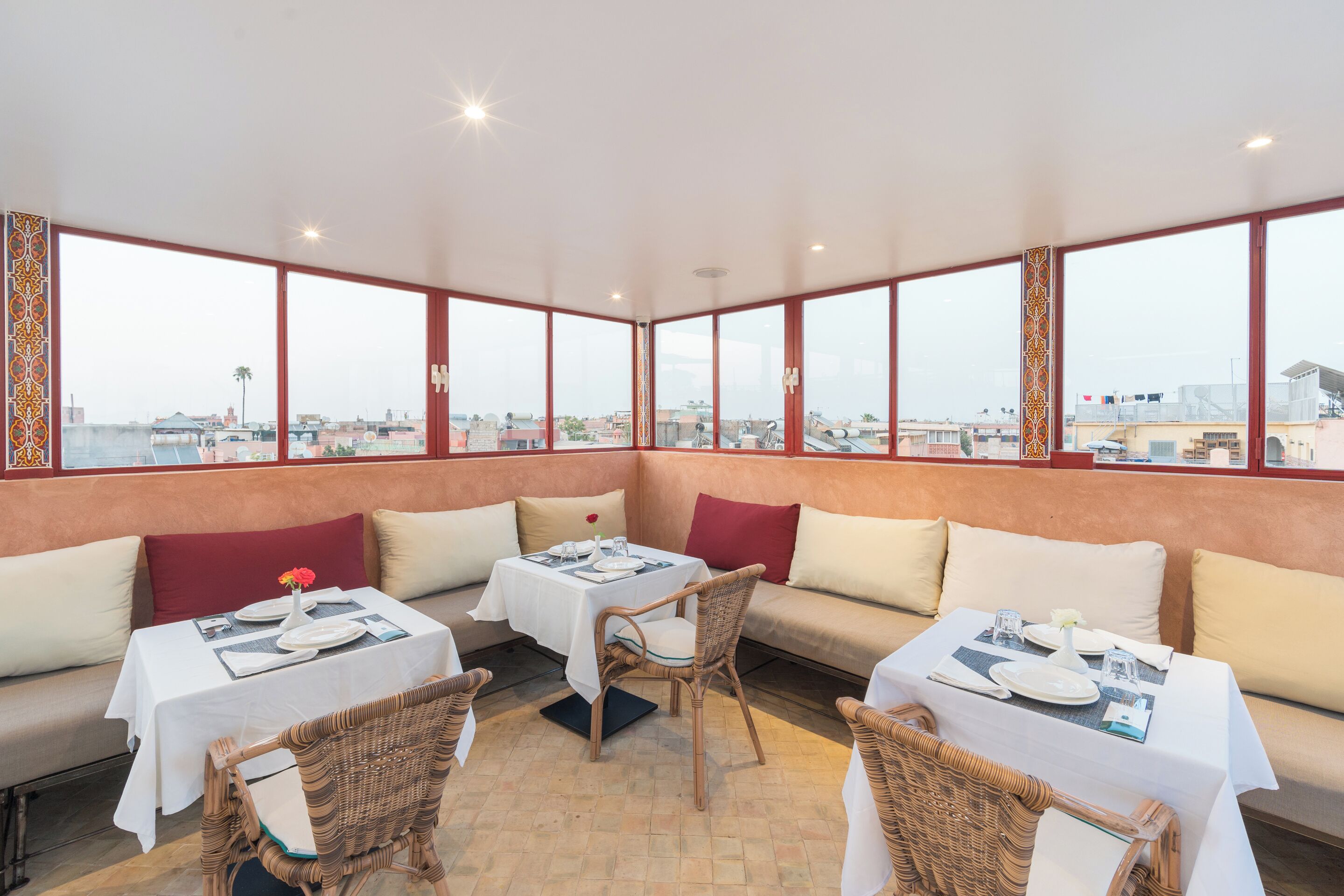 A dining area with tables and chairs, large windows with a city view, and a high ceiling.