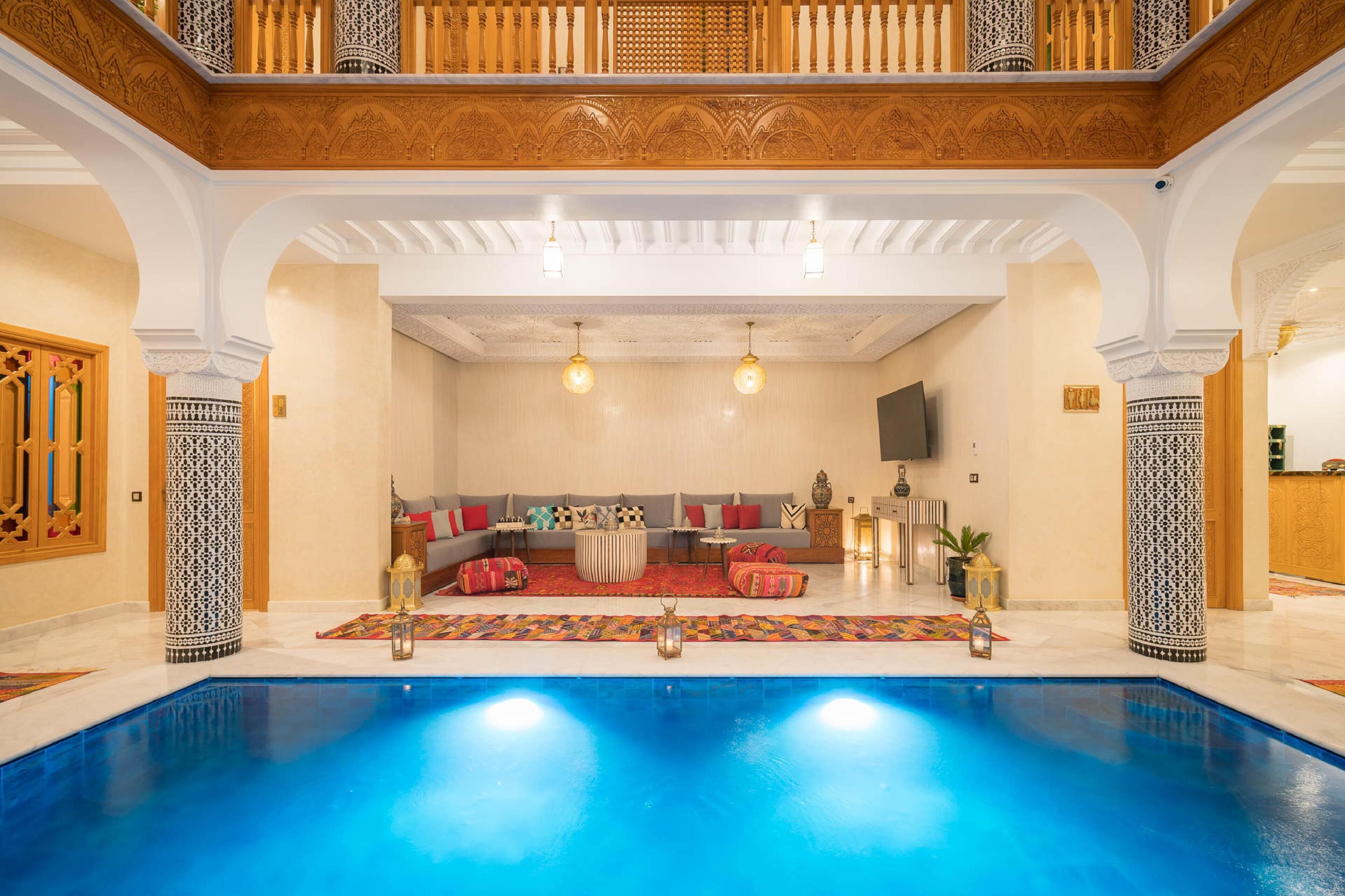 A luxurious indoor swimming pool area with a seating area, ornate columns, and a high ceiling.
