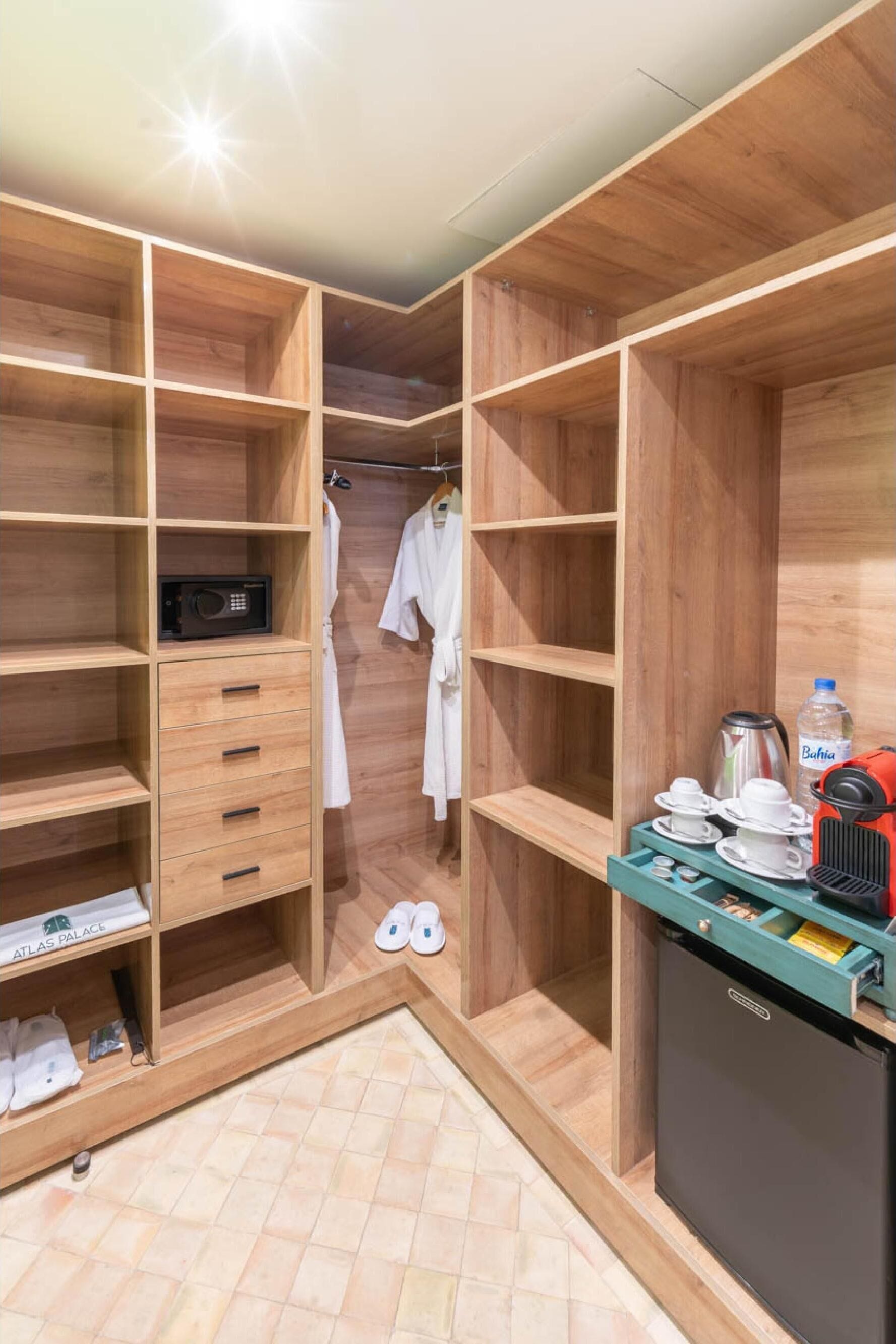 A compact hotel room with wooden shelving, a microwave, a small refrigerator, and a coffee maker.