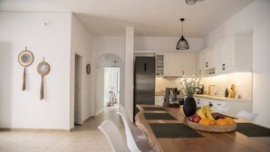 Een moderne keuken met witte kastjes, een roestvrijstalen koelkast en een eethoek met een houten tafel en witte stoelen.