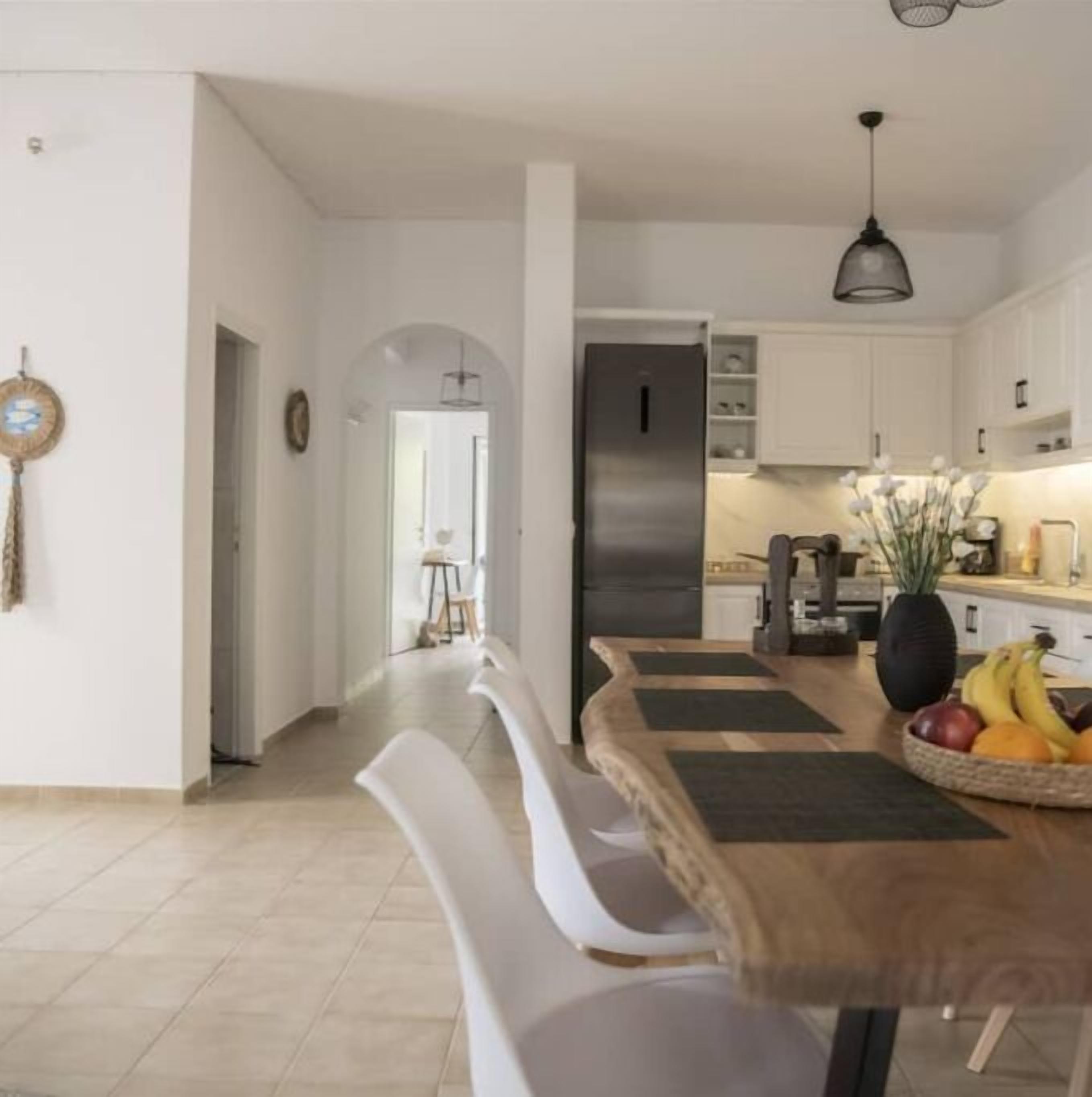 A modern kitchen with white cabinets, a stainless steel refrigerator, and a dining area with a wooden table and white chairs.