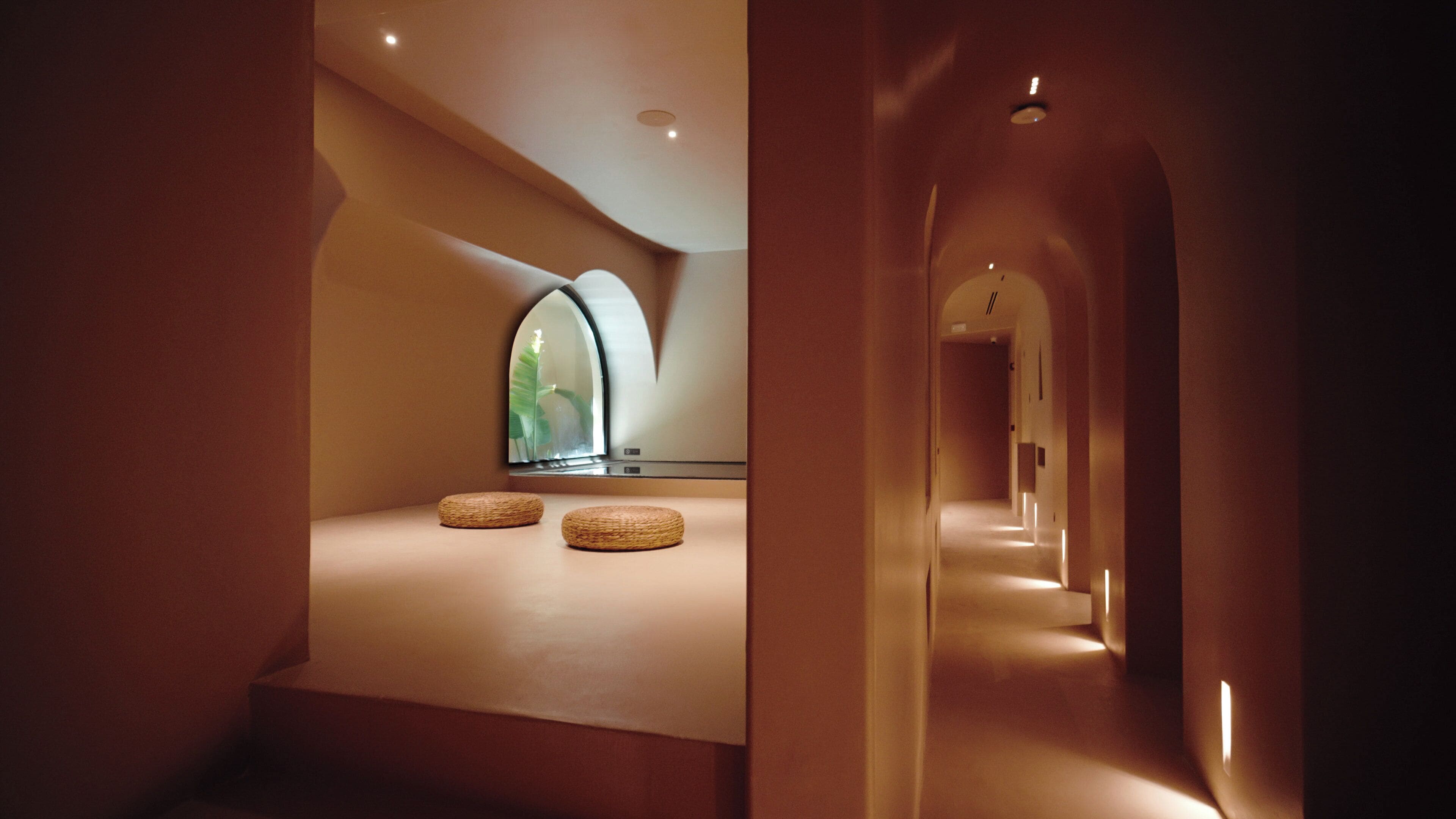 Un interior moderno con una pared curva, una zona de estar con cojines y un largo pasillo con iluminación.
