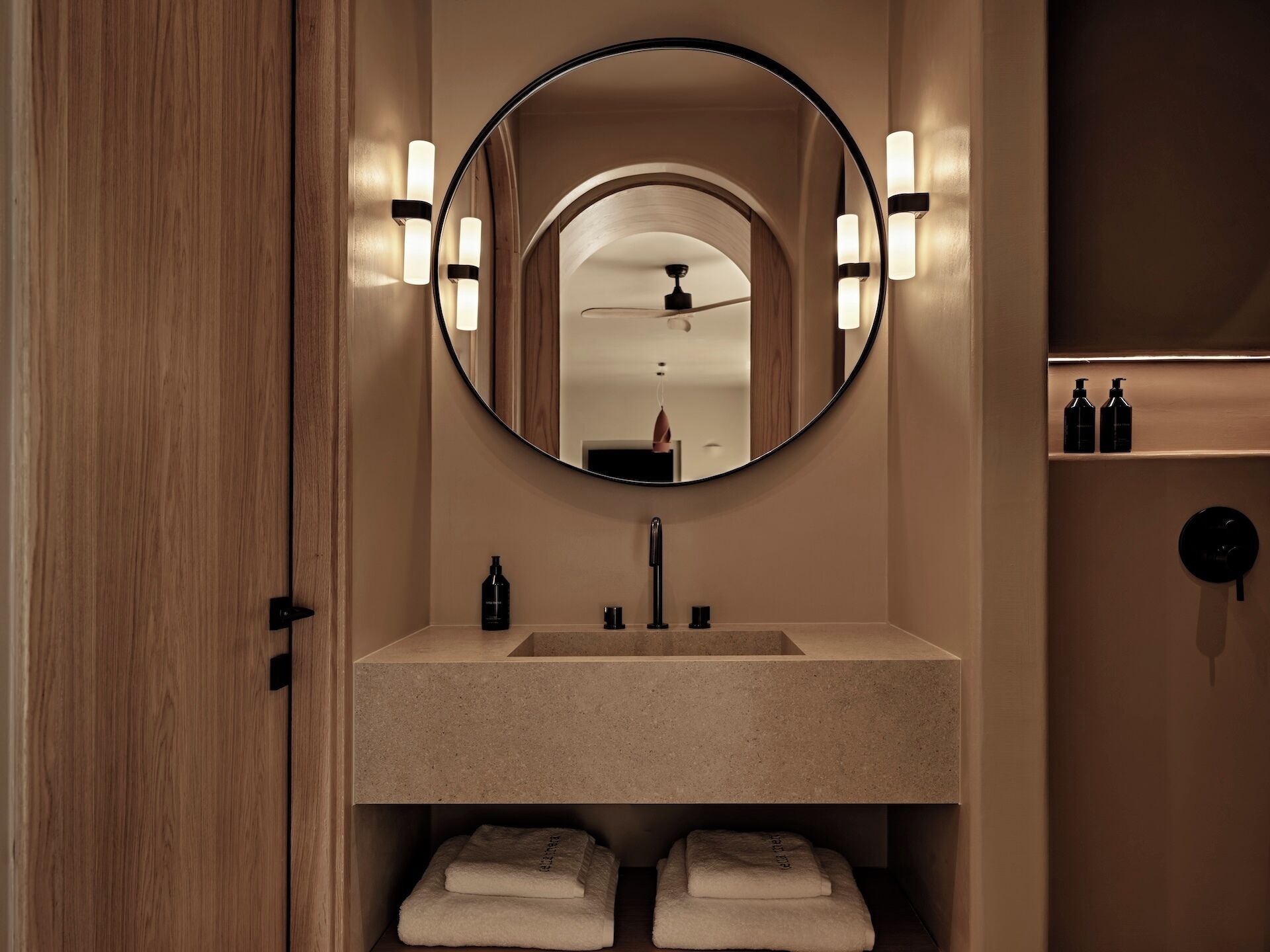 A bathroom with a round mirror, a sink, and two towels.