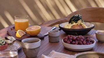 A breakfast table with a bowl of eggs, a glass of orange juice, a bowl of grapes, and a cup of coffee.