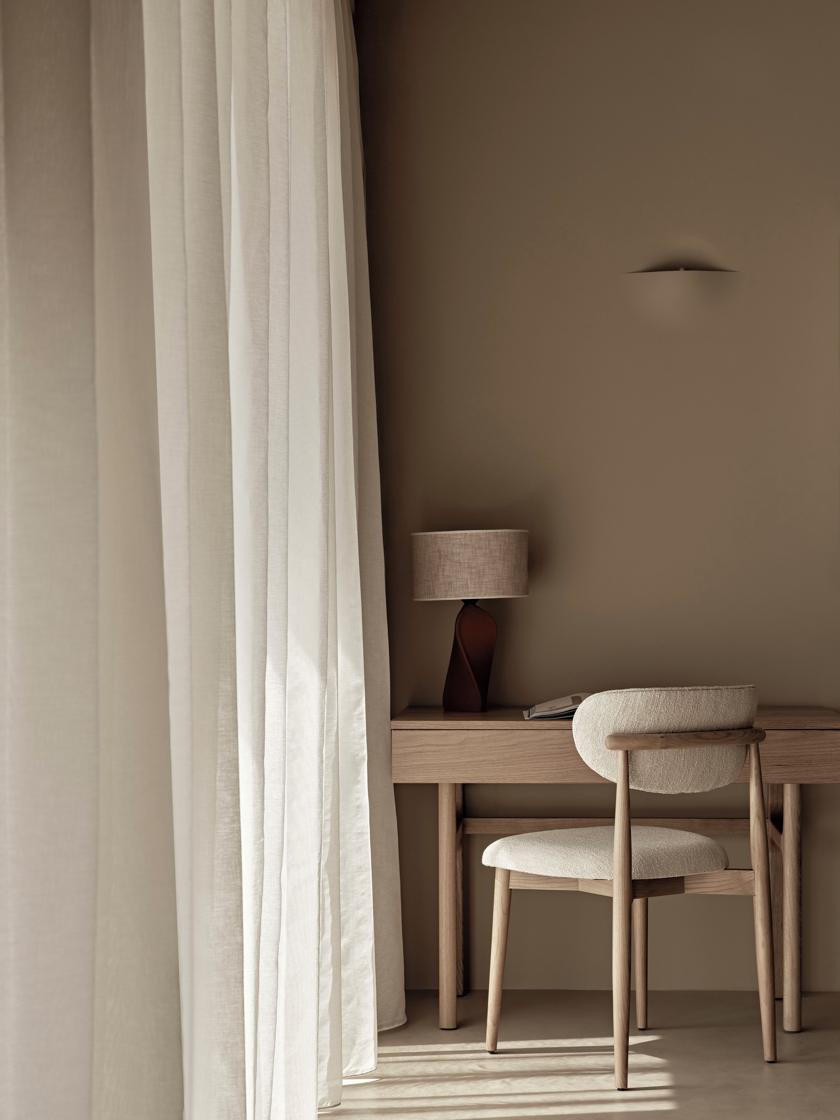 A minimalist room with a wooden desk, a chair, and a lamp.