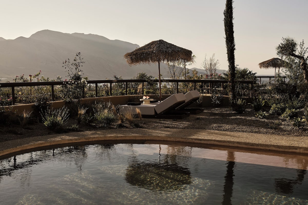 Un espace piscine agrémenté de chaises longues et de parasols, entouré de plantes et offrant une vue sur les montagnes.