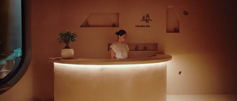 A reception desk with a potted plant, a sign reading "Thaleria Spa," and a minimalist interior design.