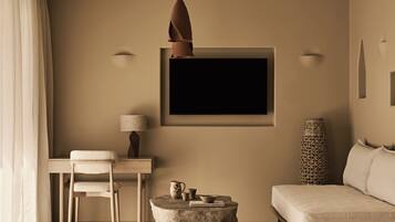 Ein modernes Wohnzimmer mit einer Couch, einem Sessel, einem Tisch, einer Pendelleuchte und einem an der Wand montierten Fernseher.