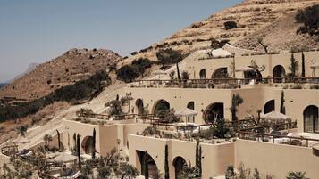 Un resort con piscina, mobiliario exterior y montañas al fondo.