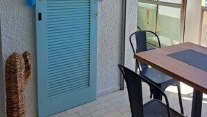 Quarto com porta azul, uma mesa e cadeiras. Vista para o oceano através de grandes janelas.